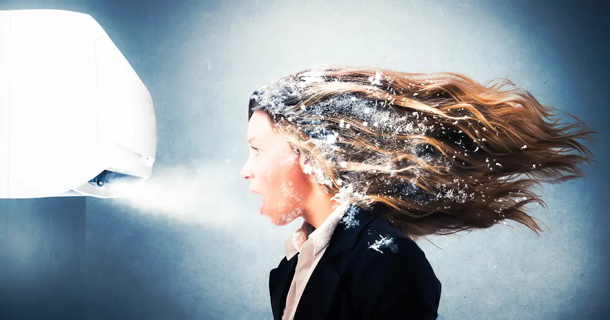 Lady in front of an Air Conditioner, frost in her hair, as she is "blown away" by the cold air.