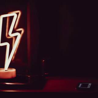 A neon lightning bolt lamp sits upon a laptop computer in the dark.