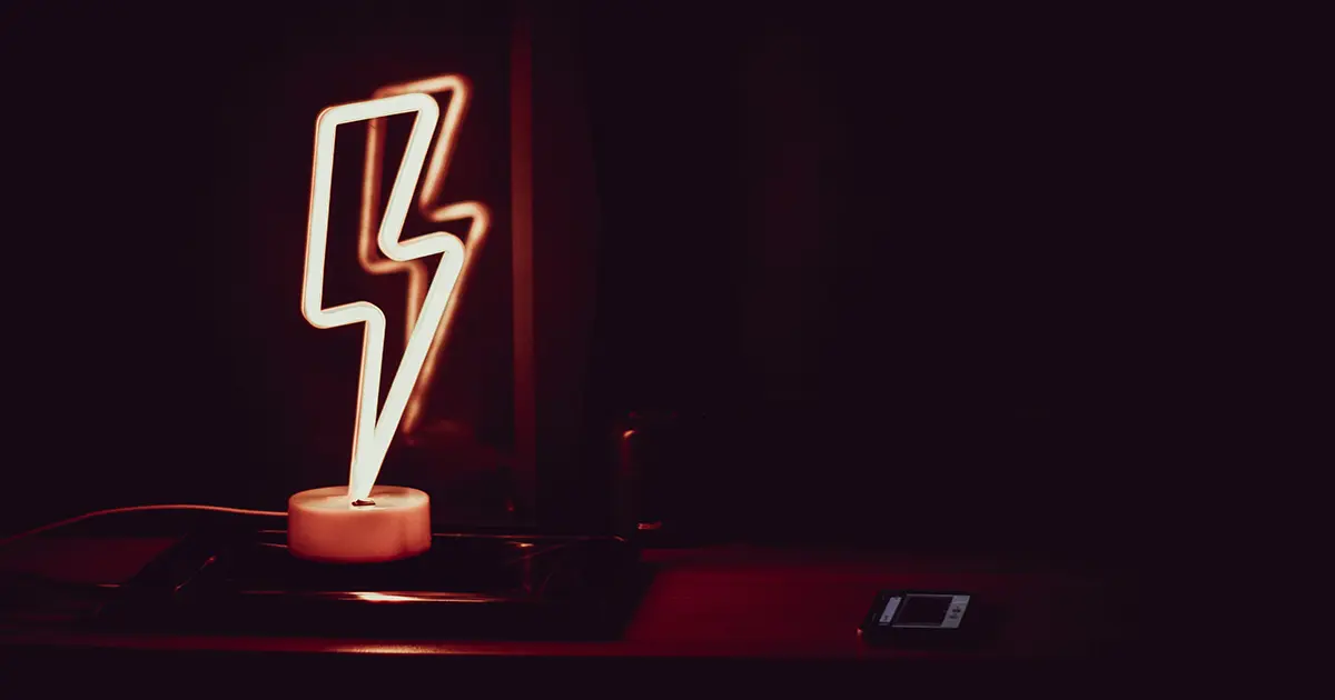 A neon lightning bolt lamp sits upon a laptop computer in the dark.