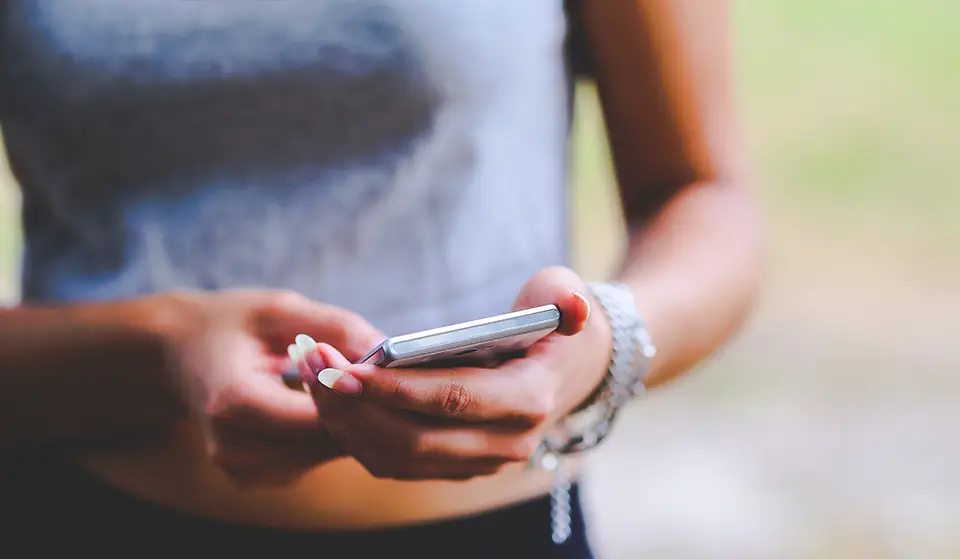 A woman uses her smartphone to adjust her smart thermostat at home.