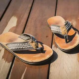 A pair of old, wet sandals, on a wooden deck.